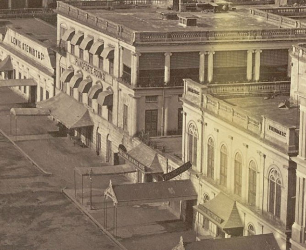 Schwarz-weiß-Foto einer Stadtstraße mit Gebäuden, Fenstern, Säulen, Namensschildern, Schuppen und Pfählen.