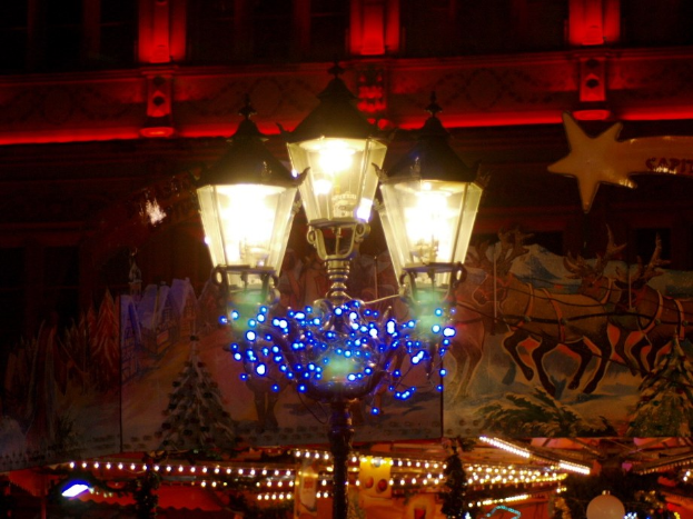 Eine festlich geschmückte Straßenlaterne in einer nächtlichen Stadt mit einem Gebäude im Hintergrund.