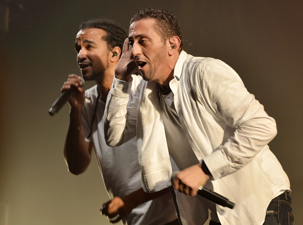 Zwei Männer in legerer Kleidung performen auf der Bühne nebeneinander, jeder hält ein Mikrofon.