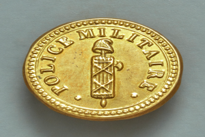 Eine Goldm├╝nze mit der Aufschrift "Police Militaire" vor einem wei├čen Hintergrund.