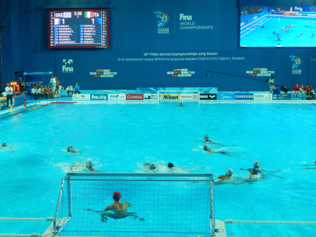Gruppe von Athleten beim Wasserballspielen in einem Pool während der FINA-Weltmeisterschaften 2016 in Kazan, mit einem Netz, das den Pool teilt, und Zuschauern auf der linken Seite.