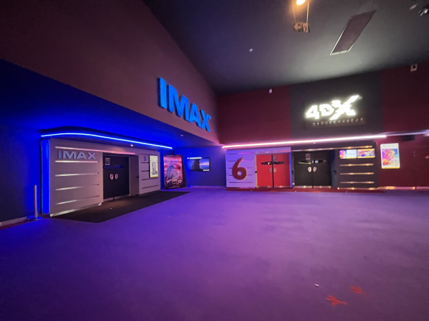 Innenseite eines Kinos mit einem violetten Teppich, Text und Bildschirmen an den Wänden und Deckenleuchten.