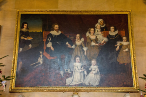 Ein gerahmtes Familienbild in einem Raum mit einem Weihnachtsbaum, flankiert von zwei Fotorahmen, mit festlichen Dekorationen unten.