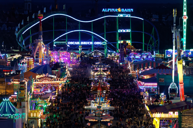 Große Menschenmenge bei nächtlichem Karneval mit bunten Lichtern, Fahrgeschäften, Pfählen, Fahnen und Namensschildern im Dunkeln