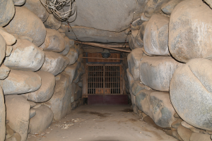 Ein tunnel voller Steine und ein Metalltor in der Mitte, mit Drähten oben, die an einen Stolleneingang erinnern.