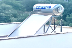 Solarwassererhitzer mit Speicher auf einem Gebäude auf dem Dach montiert, umgeben von Bäumen im Hintergrund.