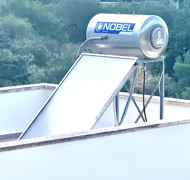 Solarwassererhitzer mit Speicher auf einem Gebäude auf dem Dach montiert, umgeben von Bäumen im Hintergrund.