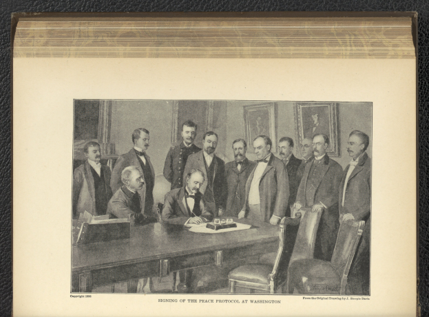 Gruppe von Männern, die um einen Tisch stehen, mit einem Mann, der in der Mitte sitzt, Papieren und Gegenständen auf dem Tisch, Rahmen an der Wand im Hintergrund und Text, der unten 'Unterzeichnung des Friedensprotokolls in Washington' lautet.