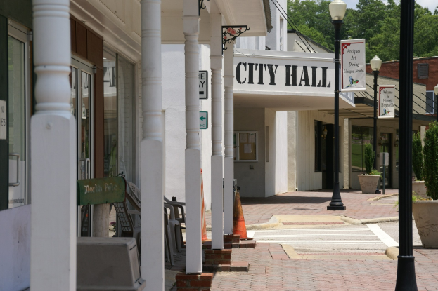 Stadthaus mit umgebender Infrastruktur, einschließlich Straßenlaternen, Schildern, Fahrzeugen, Verkehrskegeln, Stühlen, Topfpflanzen, Bäumen und einer bewölkten Himmel.