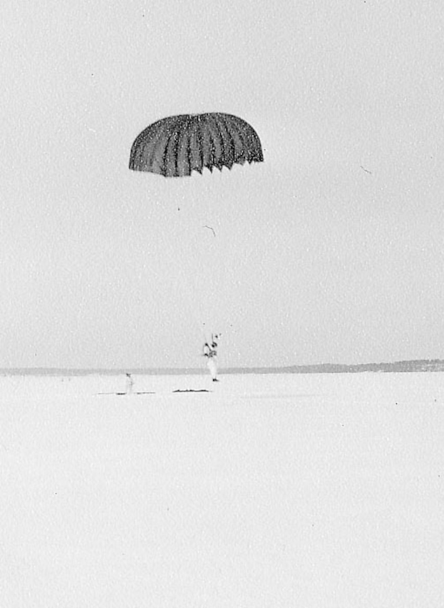 Eine Person mit einem Fallschirm am Himmel, dargestellt in Schwarz-Weiß.