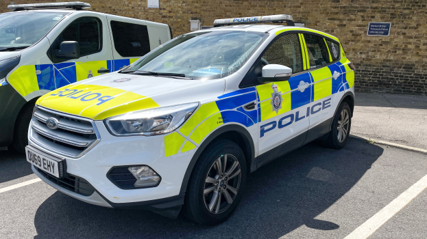 Zwei Polizeiautos nebeneinander auf einem Parkplatz geparkt, mit einer Wand und einem Schild im Hintergrund.