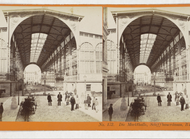 Ein altes Foto eines belebten Bahnhofs mit Menschen, Pferdewagen und Gebäuden im Hintergrund, mit Text am unteren Bildrand.