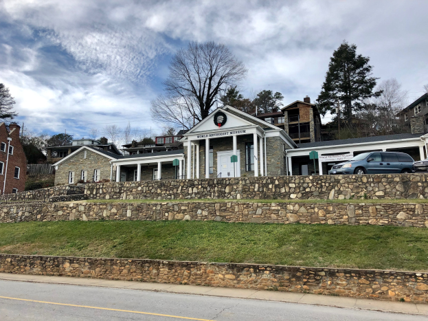Steinmauer mit geparkten Autos, angrenzende Gebäude mit Fenstern und Türen, Bäume und ein bewölkter Himmel im Hintergrund, als Weltkulturerbe-Museum bezeichnet.