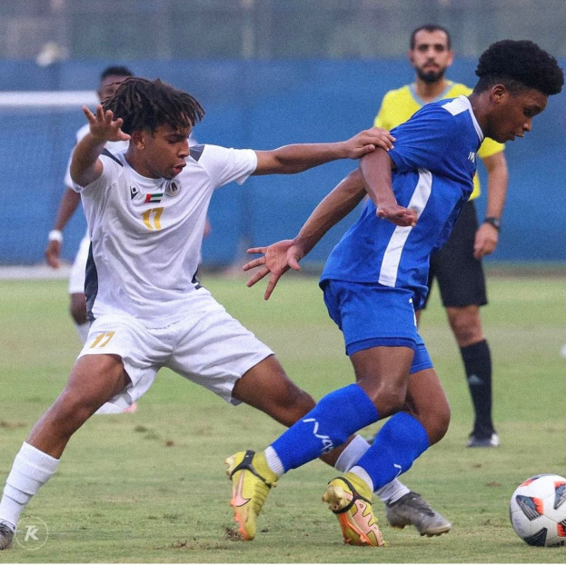 Zwei Männer spielen Fußball auf einem Rasenfeld, wobei einer zu siegen scheint.