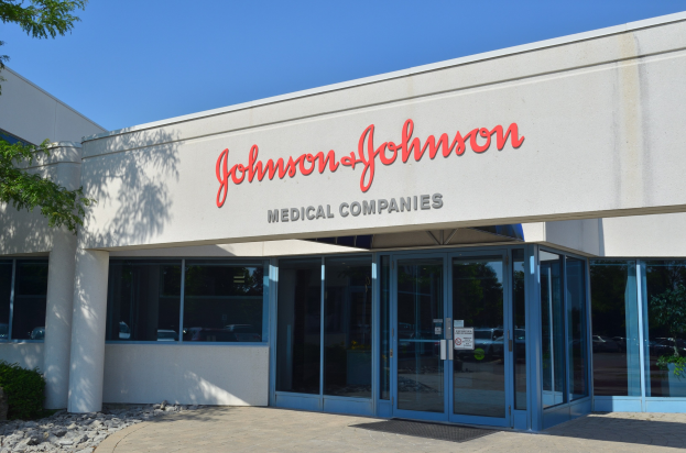 Das Johnson & Johnson Medical Companies-Gebäude mit Glaswänden und -türen, Text an der Wand, Steinen, Pflanzen und einem Baum auf der linken Seite unter einem klaren blauen Himmel.