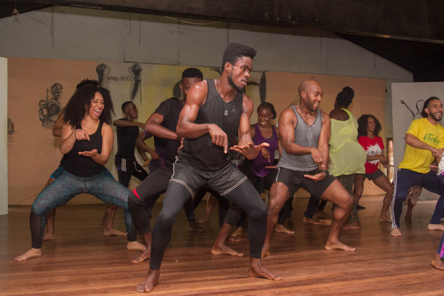 Eine Gruppe von Menschen tanzt in einem Choreografie-Kurs an der Universität Chicago, mit einer Wand im Hintergrund, die mit Gemälden geschmückt ist.