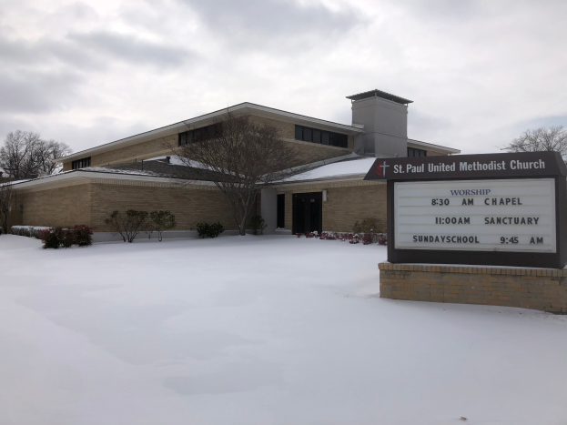 St. Paul United Methodist Church, ein Gebäude mit Fenstern und Türen, umgeben von Pflanzen und Bäumen, mit Schnee auf dem Boden und einem bewölkten Himmel im Hintergrund; ein Schild mit Text ist auf der rechten Seite des Bildes zu sehen.