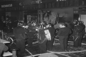 Schwarzes Bild von Feuerwehrleuten in Uniform mit Beatmungszylindern, die neben einem Fahrrad und einem Tisch mit Gegenständen stehen.