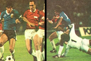 Eine Gruppe von Männern beim Fußballspielen auf einem Feld, wobei einer den Ball tritt und andere versuchen, die Kontrolle zu erlangen, vor einer Tafel in einem Stadion.