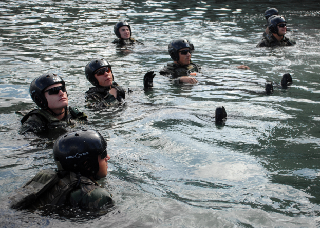 Eine Gruppe von Menschen in Helmen und Schwimmbrillen schwimmt in ruhigem, klarem Wasser unter strahlendem Sonnenschein in die gleiche Richtung.