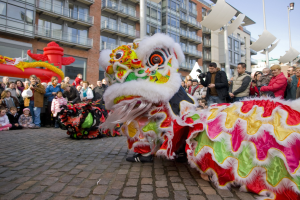 Tanz der Löwen bei einer Chinesischen Neujahrsfeier in Amsterdam, mit einer Zuschauermenge und Gebäuden im Hintergrund.