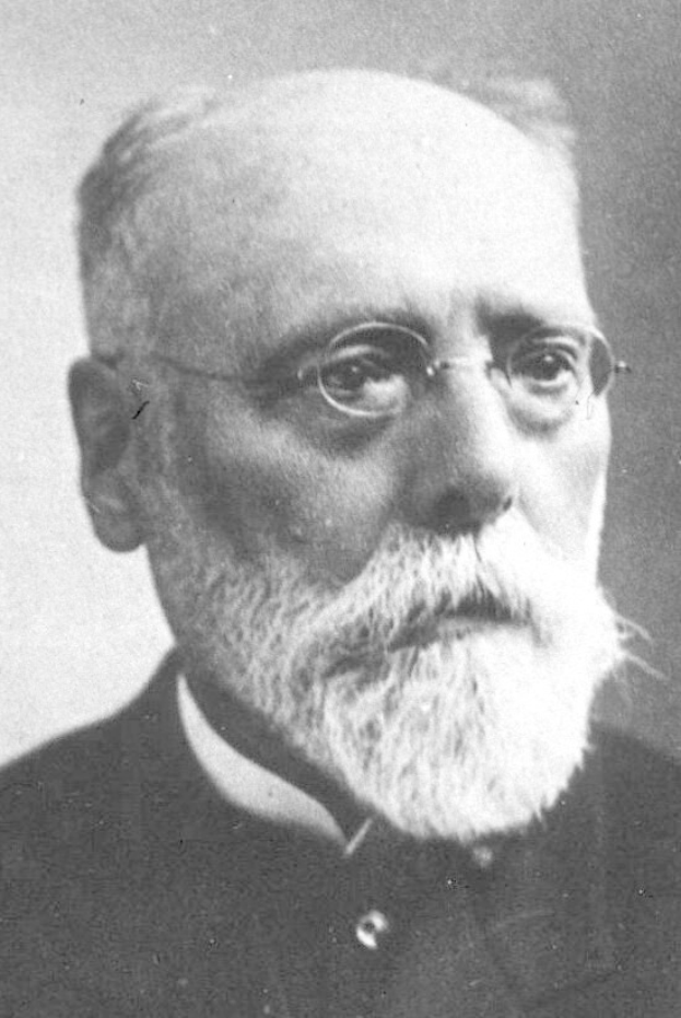 Schwarzes und weißes Porträt eines Mannes mit weißem Bart, der ein schwarzes Kleid und eine Brille trägt und einen ernsten Gesichtsausdruck hat.