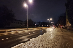 Eine Stadtstraße bei Nacht mit Straßenlaternen, die die Straße, Gehwege, Geländer, Bäume, Gebäude und andere Gegenstände beleuchten, mit dem Himmel im Hintergrund.