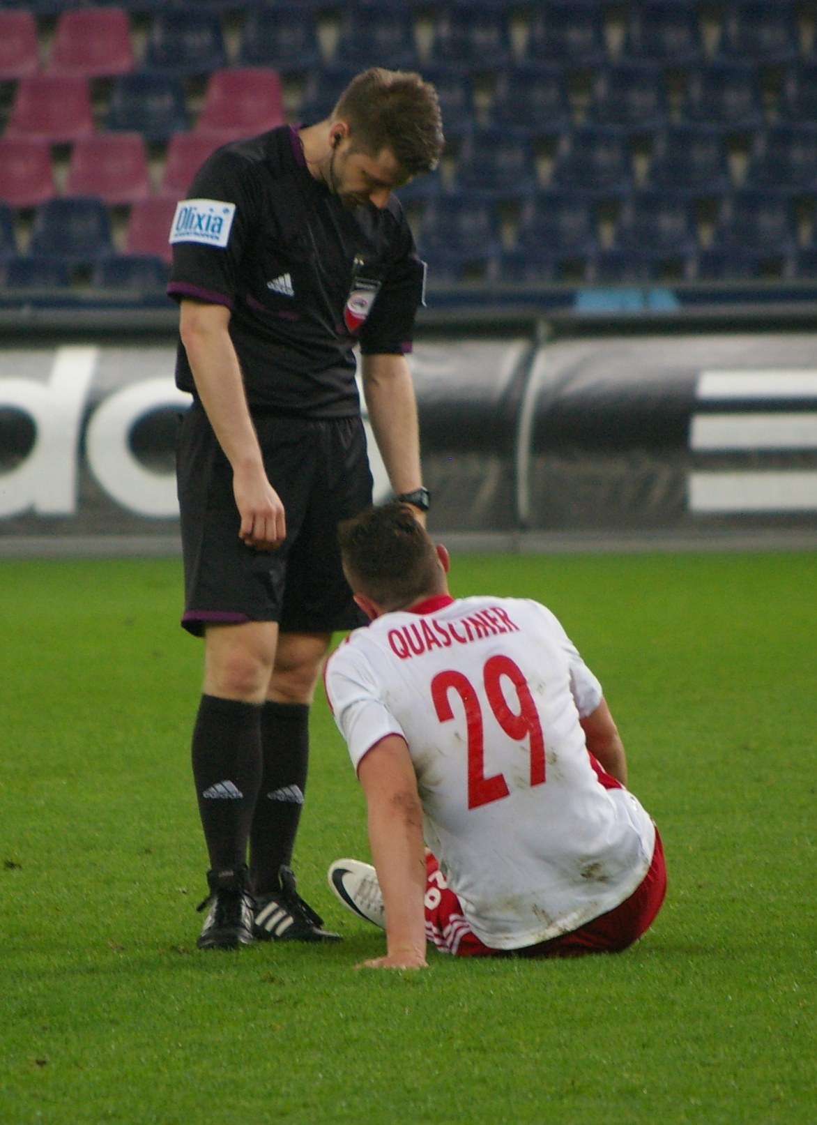 Ein Fußballspieler und Schiedsrichter sitzen auf dem Boden in einem Stadion, beide in Sportkleidung.