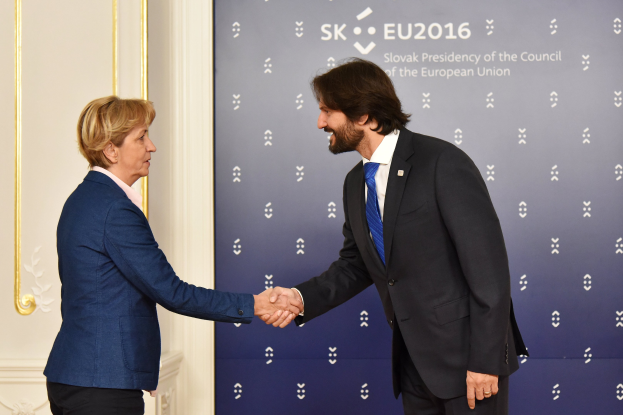 Bundeskanzlerin Angela Merkel und Joachim Gauck schütteln Hände vor einer Wand mit einem "EU-Gipfel"-Banner und einer Tür im Hintergrund, beide lächeln.