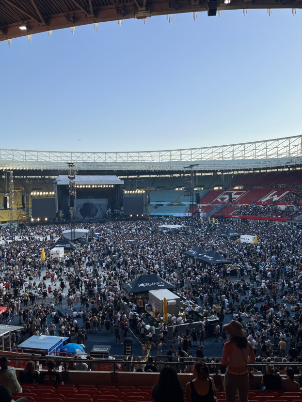 Große Menschenmenge auf Tribünen und im Stehen in einem Stadion mit Zelten, Geländern und Scheinwerfern am Himmel, mit dem Hintergrundhimmel in einem Konzert in der O2 Arena in London.