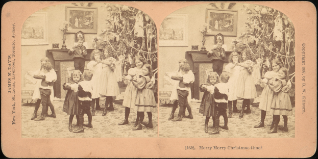 Eine Gruppe von Kindern steht vor einem Weihnachtsbaum mit einem Mann und einer Frau in der Mitte, umgeben von Rahmenfotos an der Wand.