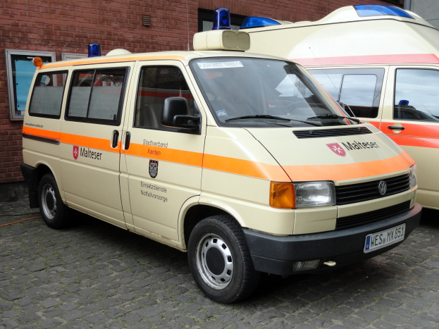 Zwei weiße Rettungswagen nebeneinander vor einem Backsteinbau mit Fenstern und einer Tür geparkt, unter einem sichtbaren Himmel.