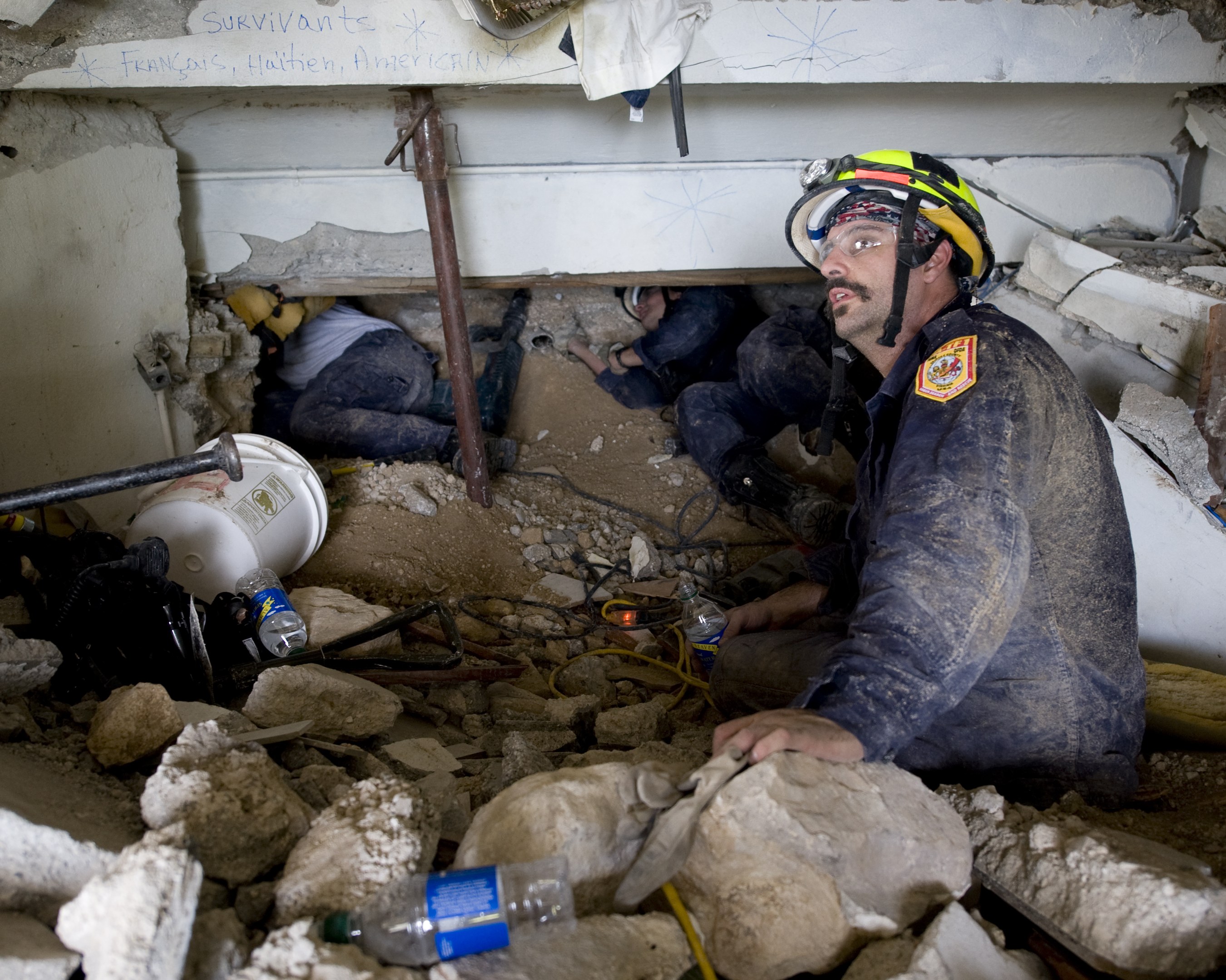 Feuerwehrmann mit Helm sitzend in Trömmern eines eingestürzten Gebäudes mit Schutt, einschließlich Flaschen, an einer israelischen Luftschlagstelle mit einem sichtbaren Gebäudename an der Wand.