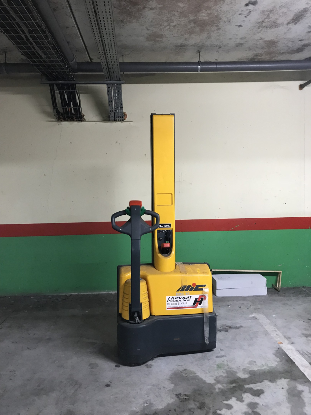 Ein gelber Gabelstapler in einem Lager mit Metallregalen auf der linken Seite und einer Wand im Hintergrund.