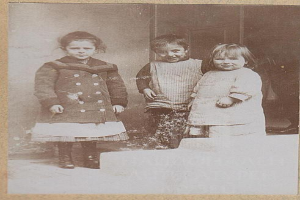 Drei Kinder auf einem alten Schwarz-Weiß-Foto stehen nebeneinander an einer Wand, ihre Gesichter scheinen traurig und hoffnungslos.