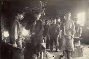 Eine Gruppe von Männern in einer Schmiede, jeder hält einen Hammer, auf einem Schwarz-Weiß-Bild.