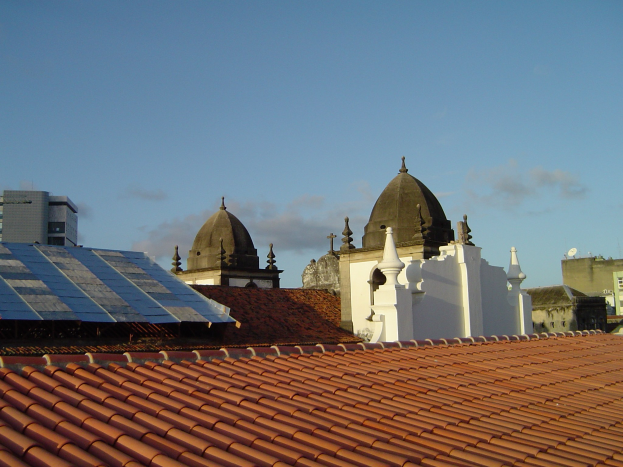 Stadtansicht mit Gebäuden im Vordergrund, einem klaren blauen Himmel im Hintergrund und Solarpanelen auf dem Dach eines Gebäudes.