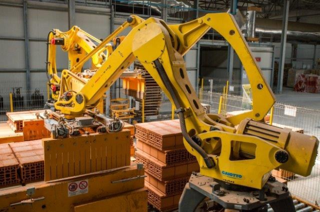 Großes Industriegebäude mit gestapelten Kisten, Kränen an der Decke, Zaun, Pfosten und einer fernen Wand in einer Fertigungsumgebung.