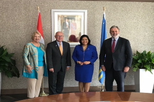 Eine Gruppe strahlender Menschen um einen Tisch mit Papieren herum, umgeben von Fahnen, Topfpflanzen und einem Foto auf der Wand, feiert die Unterzeichnung eines Memorandums zwischen den Vereinigten Staaten und Kanada.