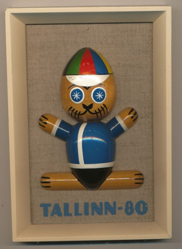 Holzspielzeug namens "Tallinn-80" in einem weißen Rahmen mit einer blauen und roten Mütze, mittig mit lesbarem Text darauf.