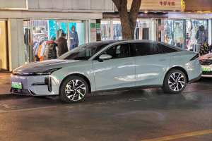 Ein Mitsubishi Lancer EV-Elektroauto, das nachts auf einer Straße geparkt ist, umgeben von Gebäuden, Geschäften, Schaufensterpuppen mit Kleidern, beleuchteten Schildern und anderen städtischen Elementen.