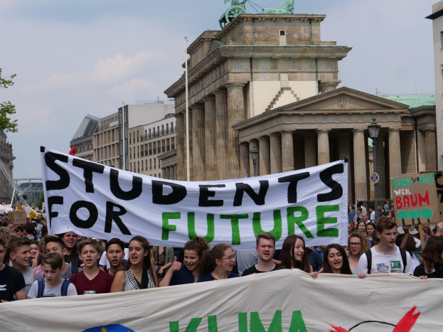 Gruppe von Schülern marschiert in Berlin mit einem buntfarbenen "Schüler für die Zukunft"-Schild gegen eine Kulisse aus Gebäuden, Bäumen und Himmel.