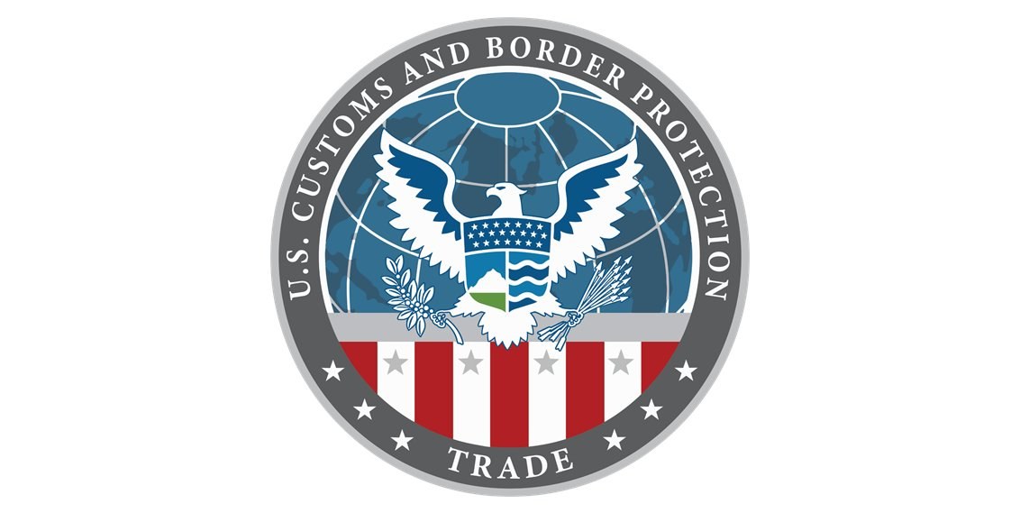 Logo des U.S. Customs and Border Protection Trade, das einen blauen Kreis mit einem weißen Stern, eine weiße Taube mit ausgebreiteten Flügeln und den Text "U.S." über der Taube zeigt, alles auf einem weißen Rand.