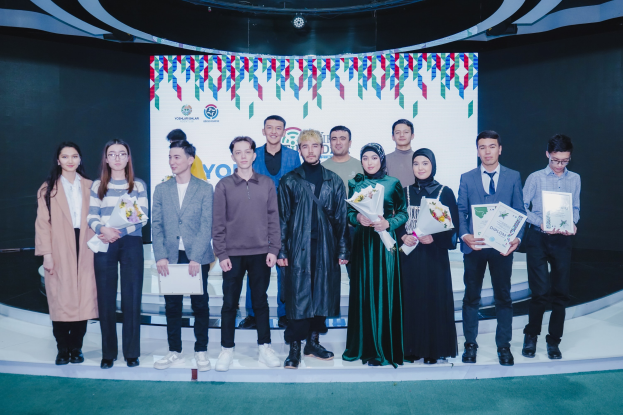 Gruppe von Menschen auf einer Bühne mit Blumensträußen und Zertifikaten, im Hintergrund ein "Jugend-Solar-Awards 2019"-Plakat.