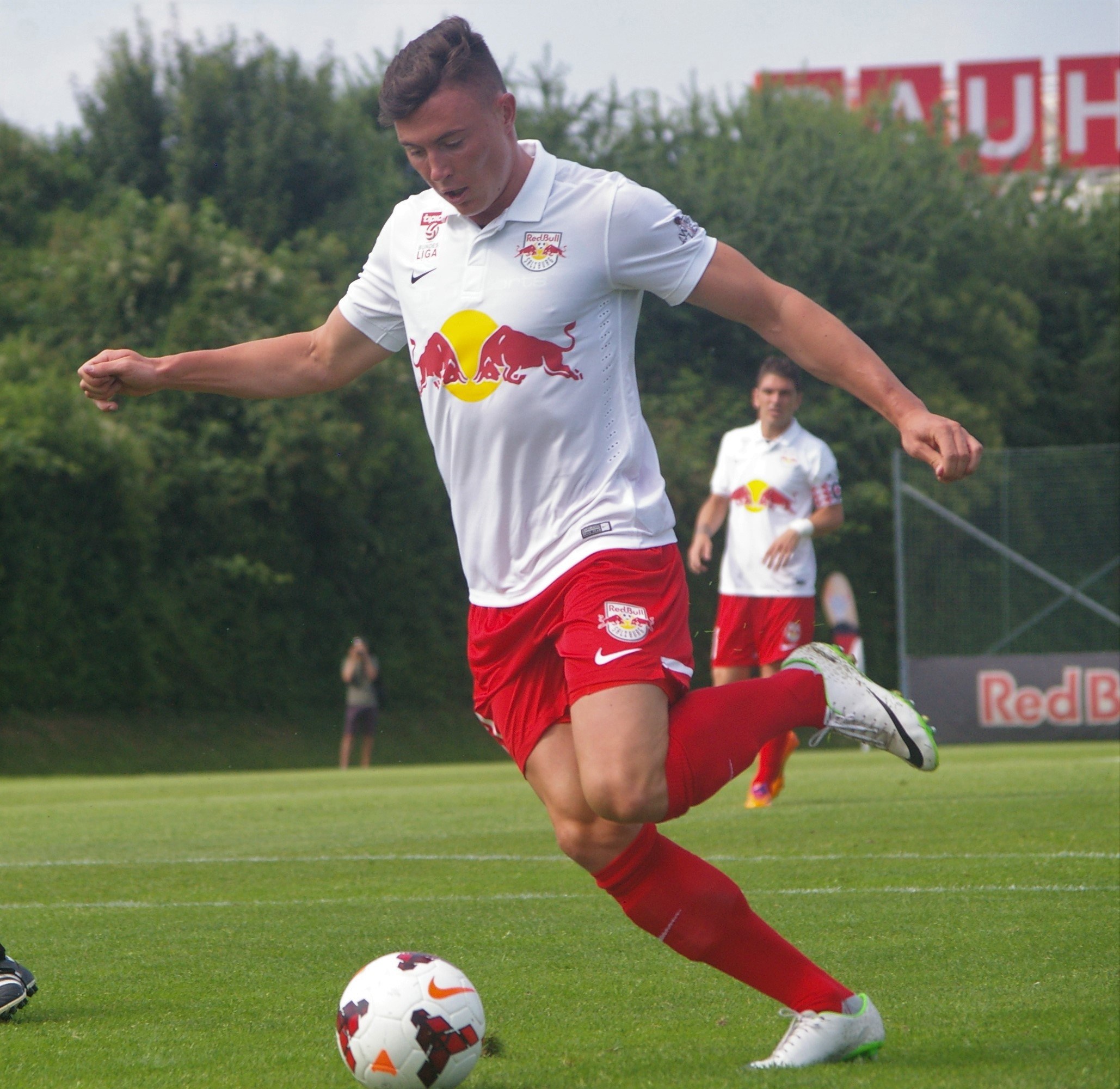 Ein professioneller Fußballspieler, der einen Ball auf einem Rasenfeld mit "RB Leipzig" im Hintergrund tritt.