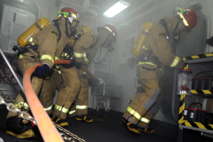Feuerwehrleute in Schutzausrüstung arbeiten in der Nähe eines Feuerwehrautos mit Ausrüstungsgestellen und sichtbaren Rohren.