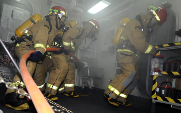 Feuerwehrleute in Schutzausrüstung arbeiten in der Nähe eines Feuerwehrautos mit Ausrüstungsgestellen und sichtbaren Rohren.