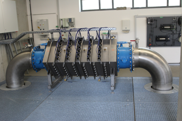 Großer industrieller Wärmetauscher in einem Gebäude mit Fenstern an der Oberseite und einer Wand im Hintergrund.