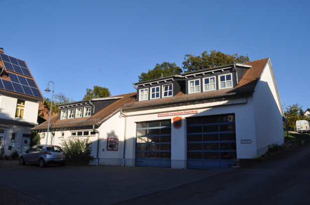 Feuerwache mit Solarpaneelen auf dem Dach, umgeben von Gebäuden, Straßeninfrastruktur, Fahrzeugen, Grünflächen und einem klaren Himmel.