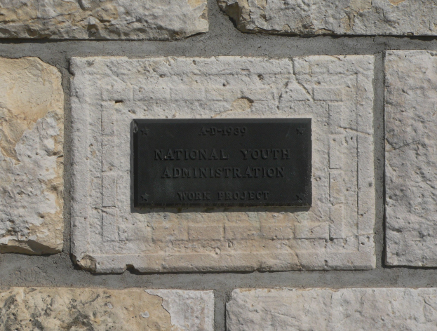 Steinwand mit einem rechteckigen Schild, auf dem in weißer, fetter, zentrierter Schrift 'National Youth Administration' steht.